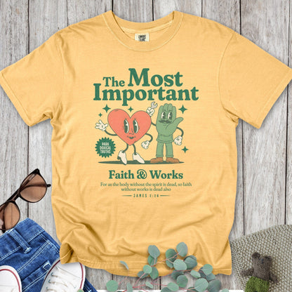 Flatlay of a Comfort Colors 1717 mustard “Faith & Works” t-shirt featuring heart and hand characters under “The Most Important” theme with James 2:26 verse. A retro-style women’s scripture tee - faith-based apparel for women and modern Christian shirt, inspiring Christian mom gift idea celebrating faith in action.