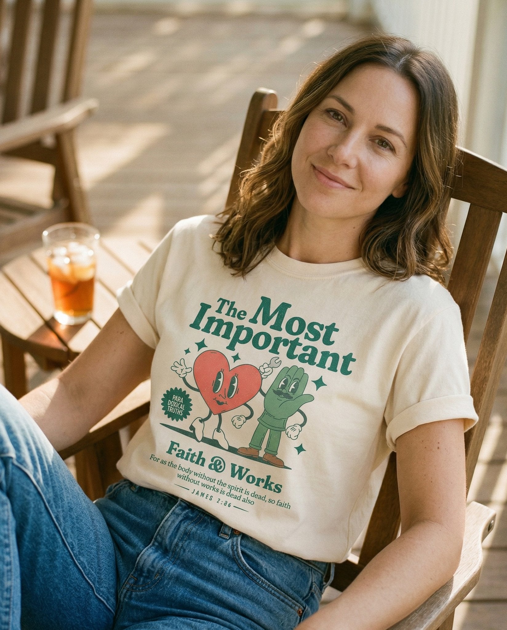 Faith and Works – Ivory women's Christian tee, lifestyle photo in sunny porch – Retro cartoon characters: an animated heart and a raised hand alongsid – James 2:26 – She Wears Faith