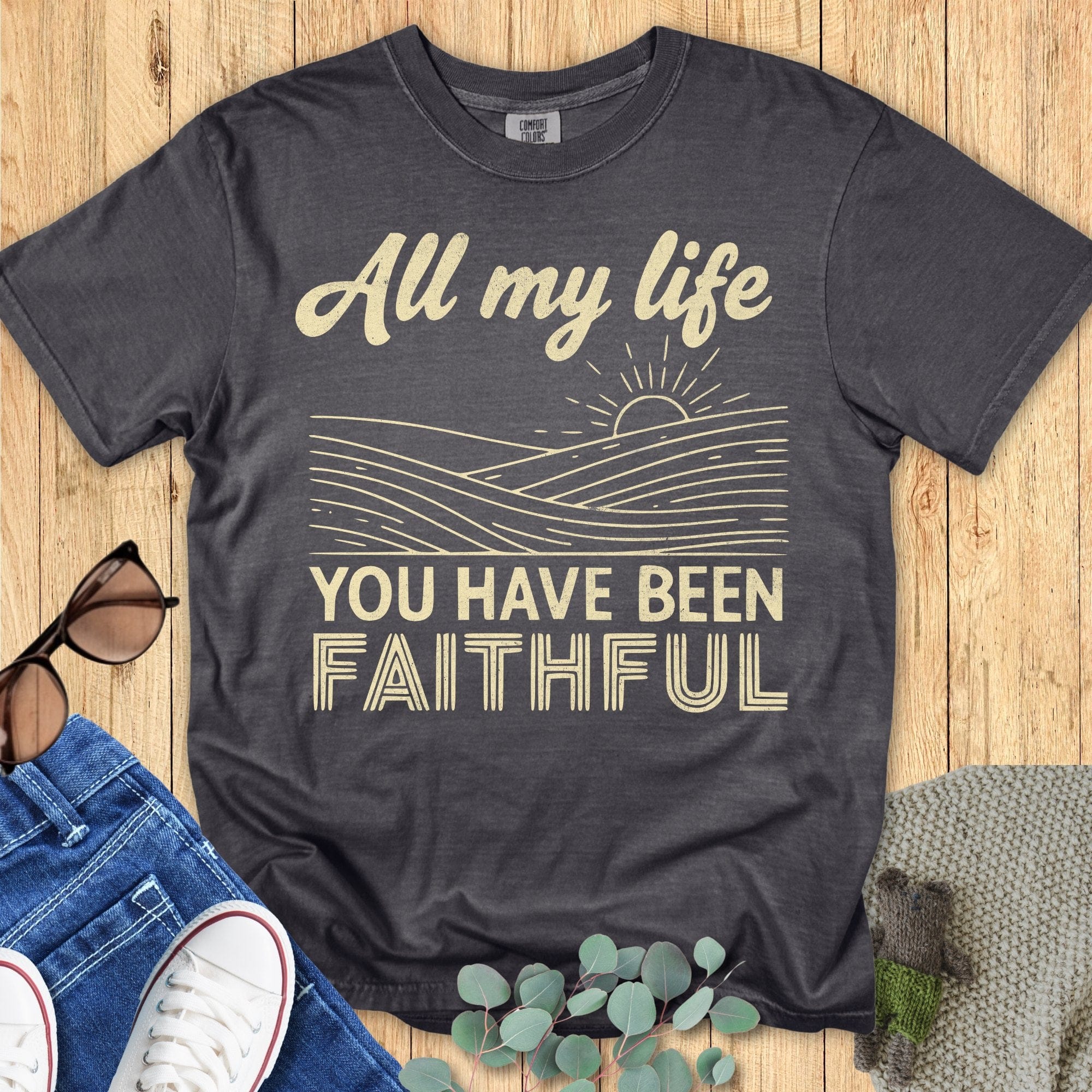 Comfort Colors 1717 Christian women t-shirt in pepper gray flat lay on wood background. Faith-based design says “All my life you have been faithful” with sunrise line ar