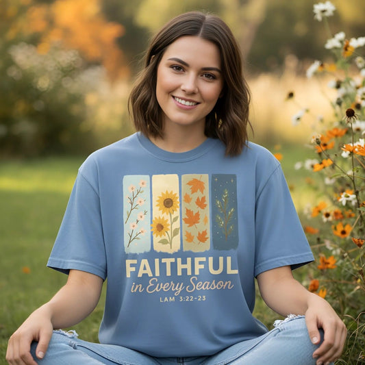 Christian women’s t-shirt on Comfort Colors 1717 in Blue Jean. A young woman sits outdoors in a garden with orange and white flowers, wearing a shirt that reads “Faithful in Every Season – Lam 3:22-23” with four seasonal panels: blossoms, sunflower, autumn leaves, and evergreen