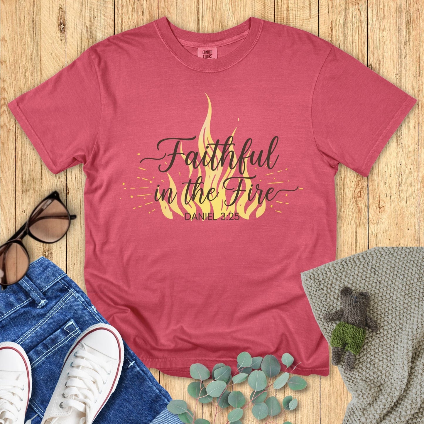 Red t-shirt with 'Faithful in the Fire' design on a wooden surface with accessories.