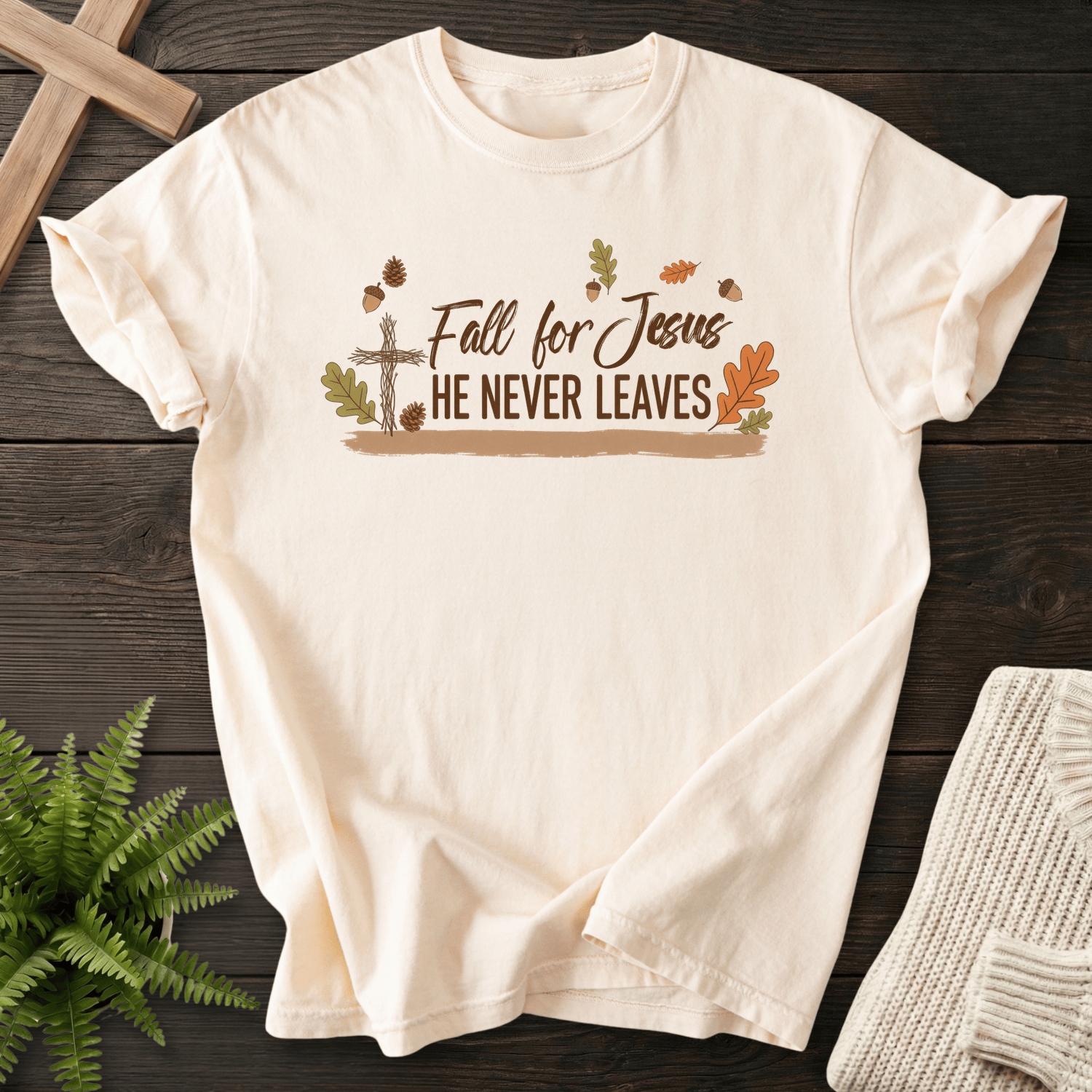 Ivory women's faith t-shirt with a rustic wooden cross, fall leaves, and acorns, featuring 'Fall for Jesus He Never Leaves'.