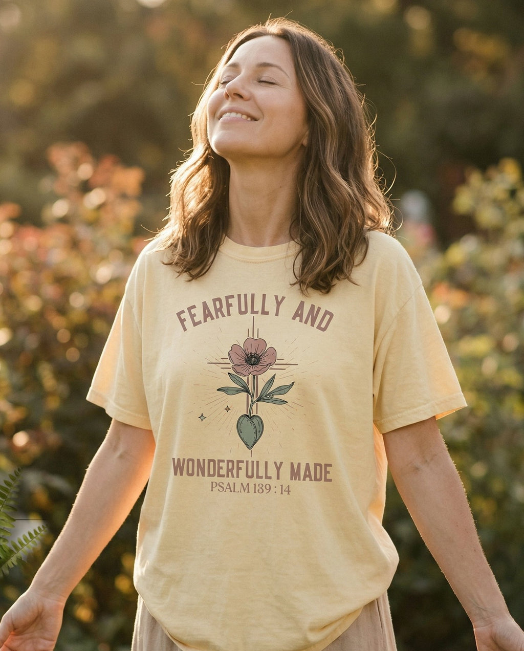 Wonderfully Made T-shirt – Banana women's Christian tee, lifestyle photo in outdoor garden – Arched lettering reading 'Fearfully And Wonderfully Made' flanking a b – Psalm 139:14 – She Wears Faith