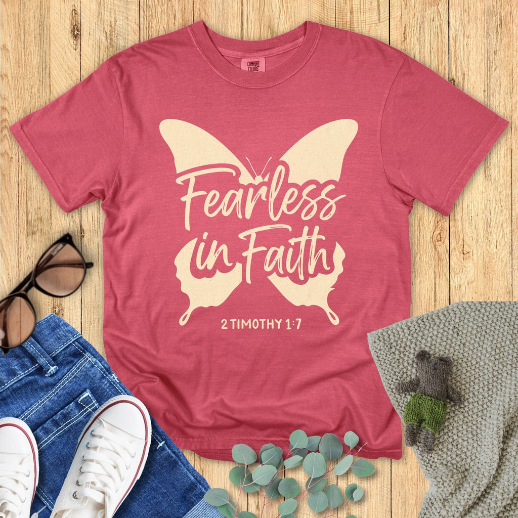 Flatlay of a Comfort Colors 1717 crimson “Fearless in Faith – 2 Timothy 1:7” t-shirt with bold cream butterfly design. A cheerful women’s scripture tee — inspiring faith-based apparel for women and modern Christian shirt, perfect Christian mom gift idea.