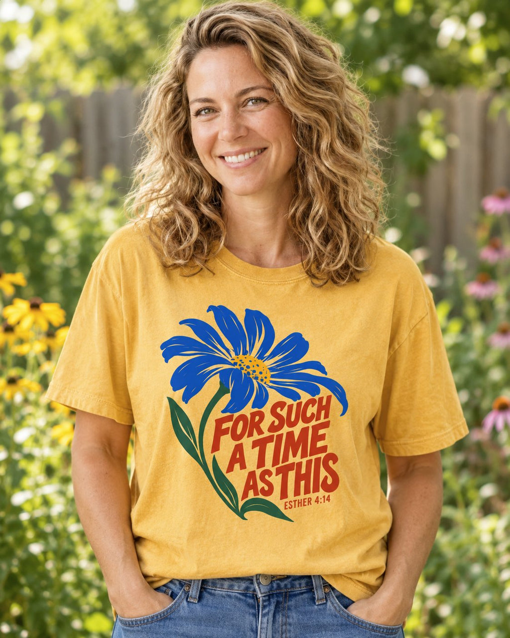 For Such a Time Daisy, Mustard women's Christian tee, lifestyle photo in outdoor garden, Blue daisy with red hand-lettered For Such A Time As This, She Wears Faith