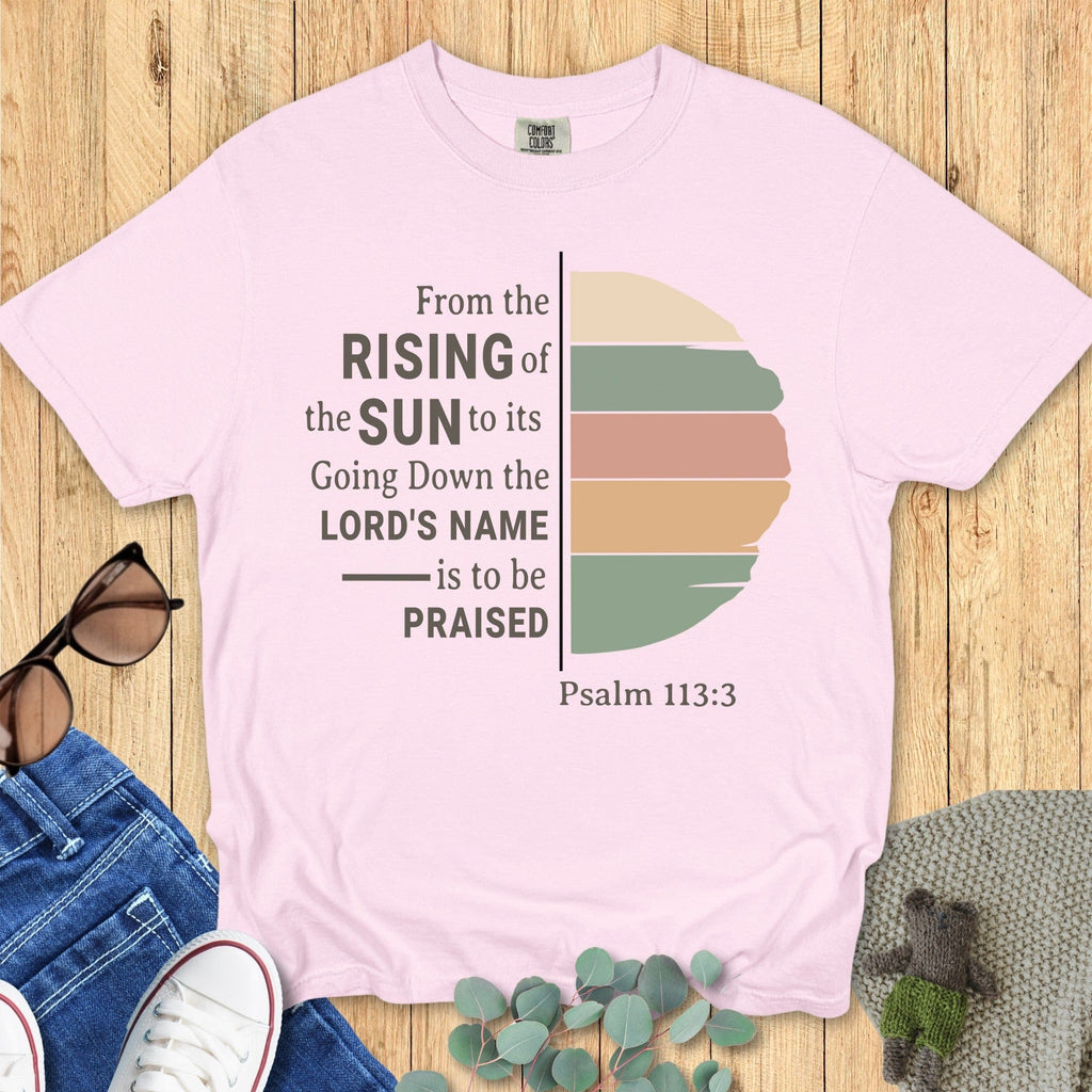 Flatlay of a Comfort Colors 1717 blossom “From the Rising of the Sun to its Going Down, the Lord’s Name is to be Praised – Psalm 113:3” t-shirt with vintage-style striped sun illustration. A feminine women’s scripture tee — faith-based apparel for women and modern Christian shirt, meaningful Christian mom gift idea.
