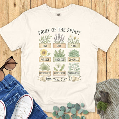 Flatlay of a Comfort Colors 1717 ivory “Fruit of the Spirit” t-shirt featuring hand-drawn botanical illustrations representing love, joy, peace, patience, kindness, goodness, faithfulness, gentleness, and self-control from Galatians 5:22–23. A soft women’s scripture tee — faith-based apparel for women and modern Christian shirt, perfect Christian mom gift idea.
