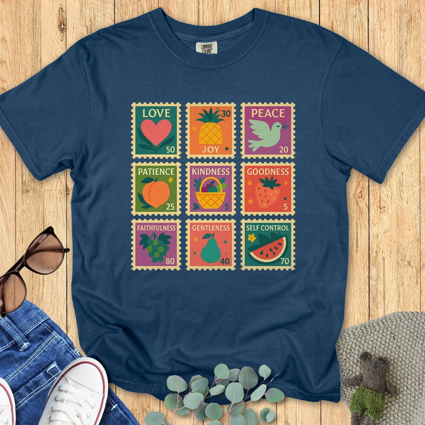 Flat lay of a Comfort Colors Christian T-shirt in midnight navy, showcasing a playful Fruit of the Spirit stamp design with vibrant fruit symbols and words: love, joy, peace, patience, kindness, goodness, faithfulness, gentleness, and self-control.