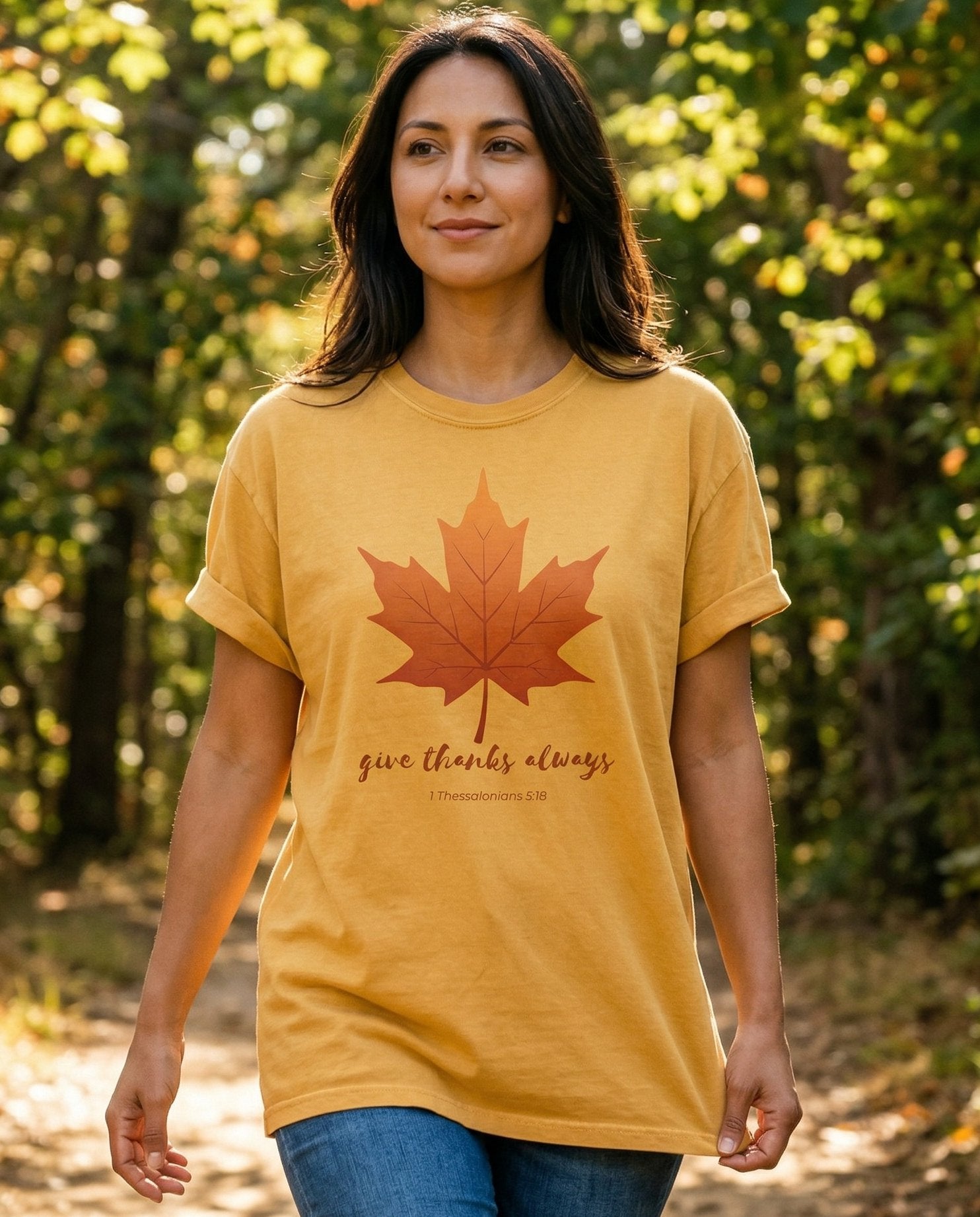 Give Thanks Always – Mustard women's Christian tee, lifestyle photo in nature trail – Illustrated autumn maple leaf in orange and red above script text read – 1 Thessalonians 5:18 – She Wears Faith