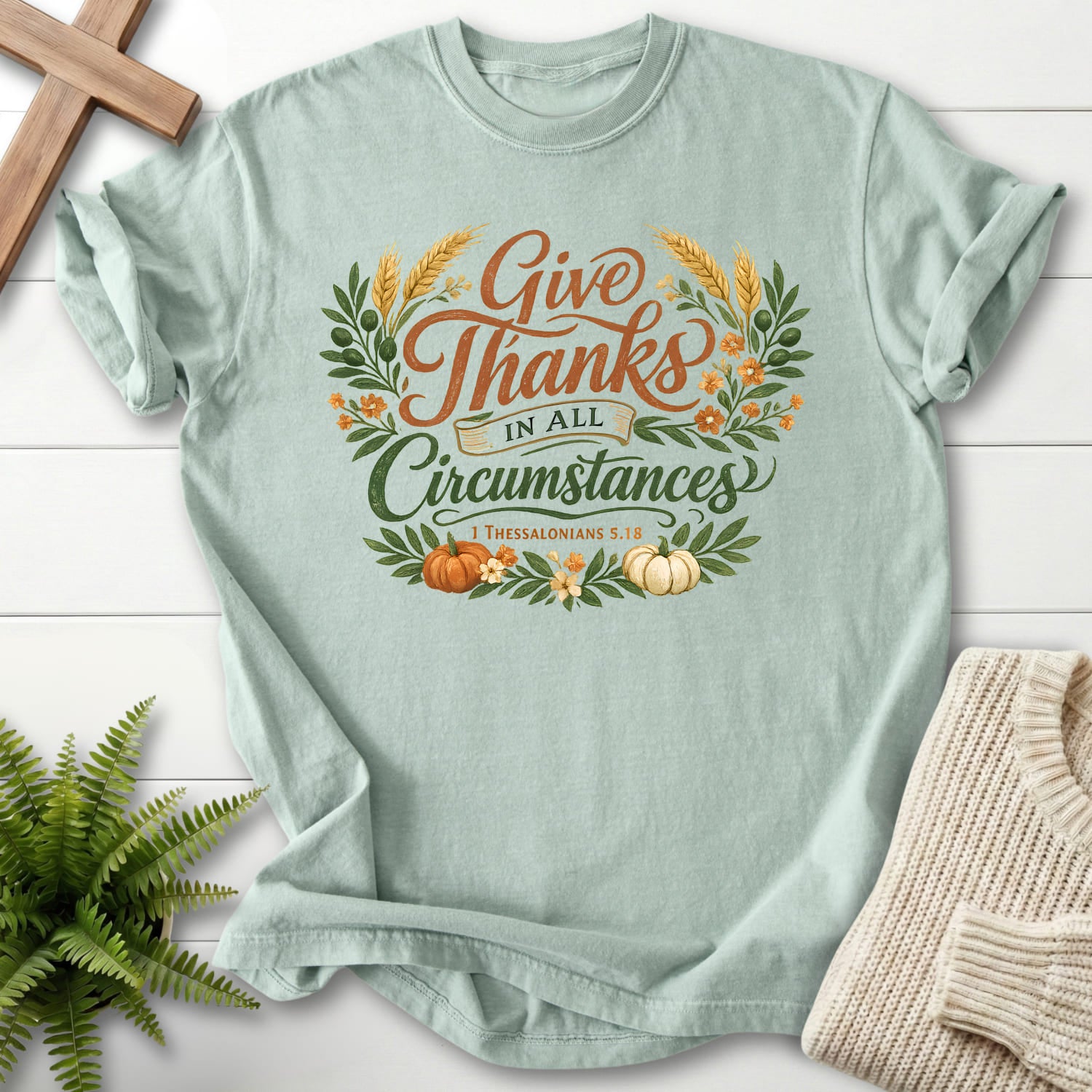 Flat lay of a Bay Christian graphic tee featuring script typography with "Give Thanks in All Circumstances T-Shirt" 1 Thessalonians 5:18.