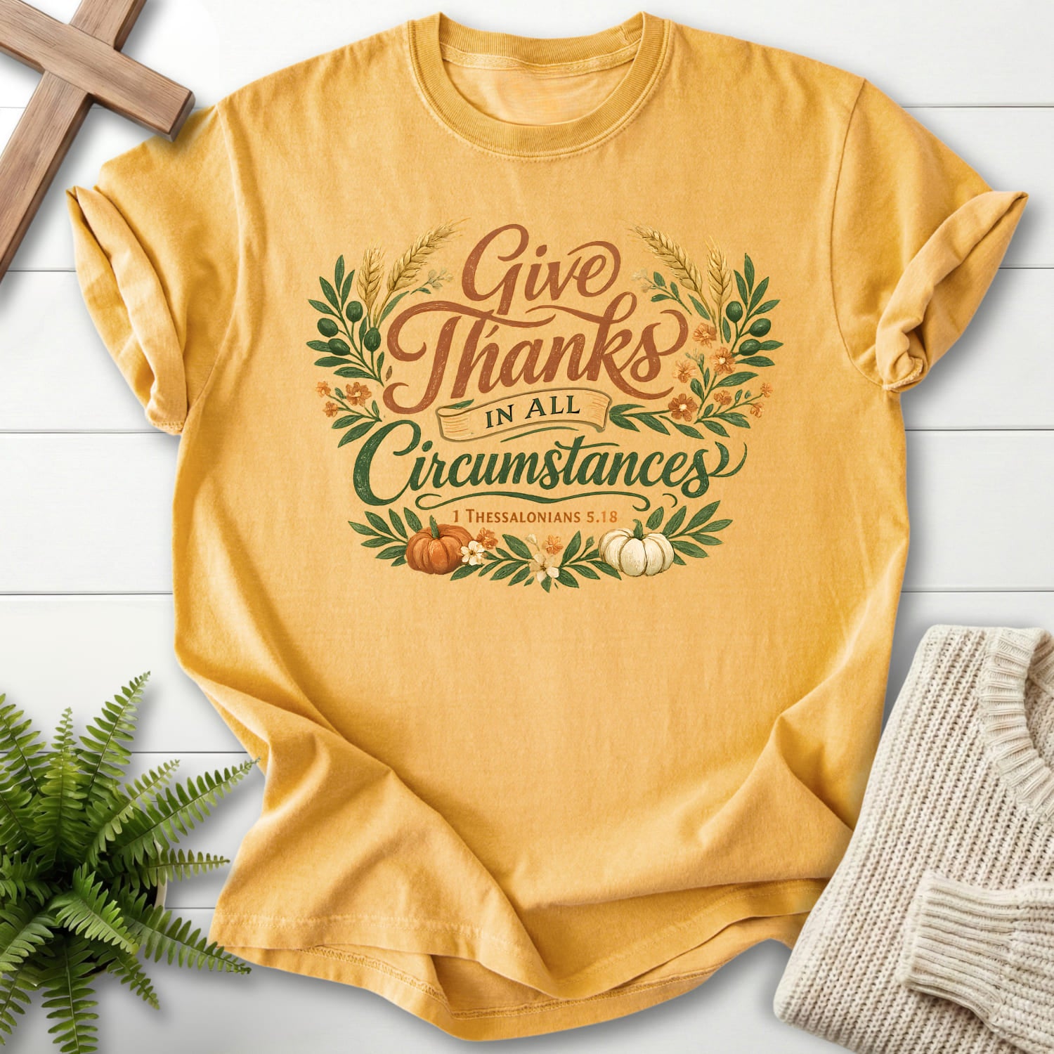 Flatlay of a Mustard Christian t-shirt for women with script typography with "Give Thanks in All Circumstances T-Shirt" 1 Thessalonians 5:18.