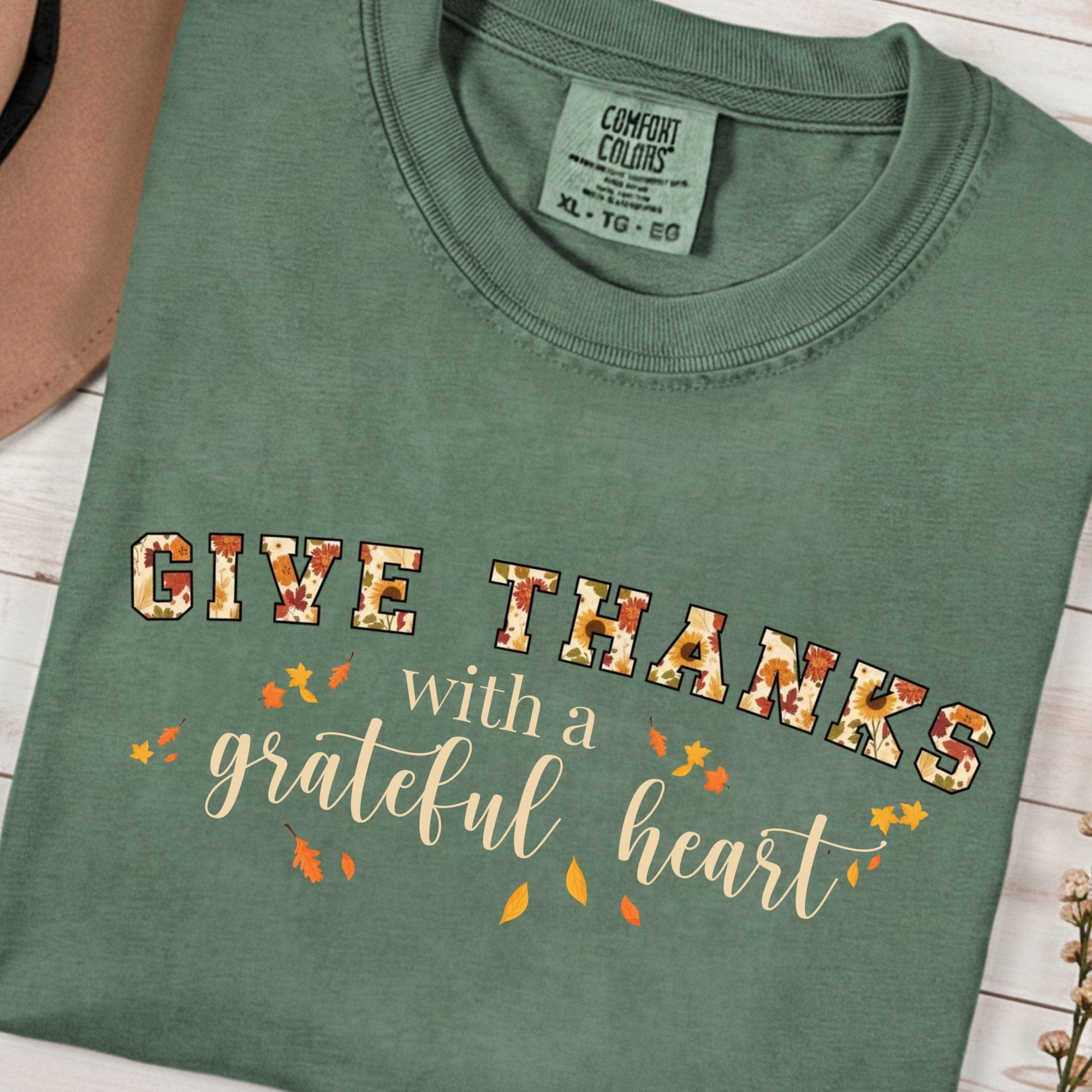 Folded Comfort Colors 1717 moss “Give Thanks with a Grateful Heart” t-shirt with vintage fall lettering and scattered leaves. A relaxed women’s scripture tee -  faith-based apparel for women and modern Christian shirt, lovely Christian mom gift idea for Thanksgiving gatherings.