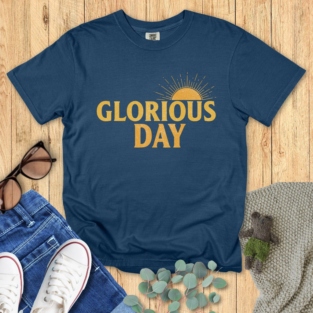 Flatlay of a Comfort Colors 1717 midnight “Glorious Day” t-shirt showcasing a warm golden sunrise graphic. A timeless women’s scripture tee — soft and inspiring faith-based apparel for women and modern Christian shirt, meaningful Christian mom gift idea.