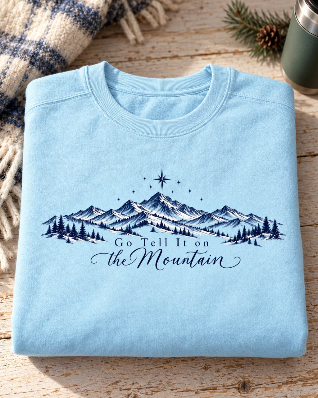 Go Tell It on the Mountain, Chambray women's Christian sweatshirt, lifestyle photo in folded flat lay, mountain range with pines and a north star, She Wears Faith