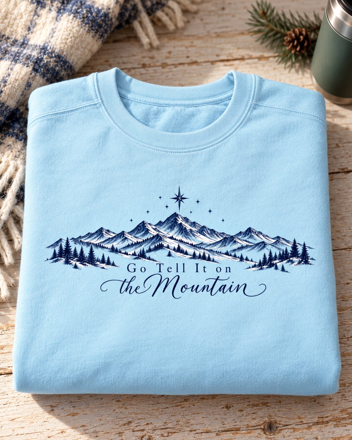 Go Tell It on the Mountain, Chambray women's Christian sweatshirt, lifestyle photo in folded flat lay, mountain range with pines and a north star, She Wears Faith