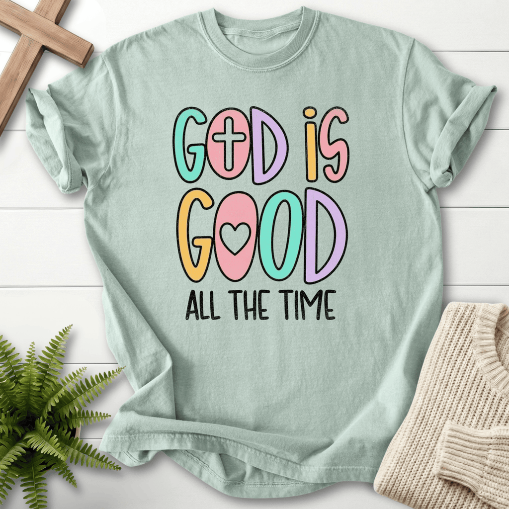 Bay blue women's faith t-shirt with bright multicolor 'God Is Good' lettering and a cross motif.