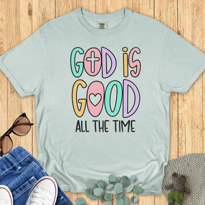 Flatlay of a Comfort Colors 1717 bay “God Is Good All The Time” t-shirt featuring pastel hand-lettered text with faith symbols. A joyful women’s scripture tee - faith-based apparel for women and modern Christian shirt, perfect Christian mom gift idea that spreads positivity and gratitude.