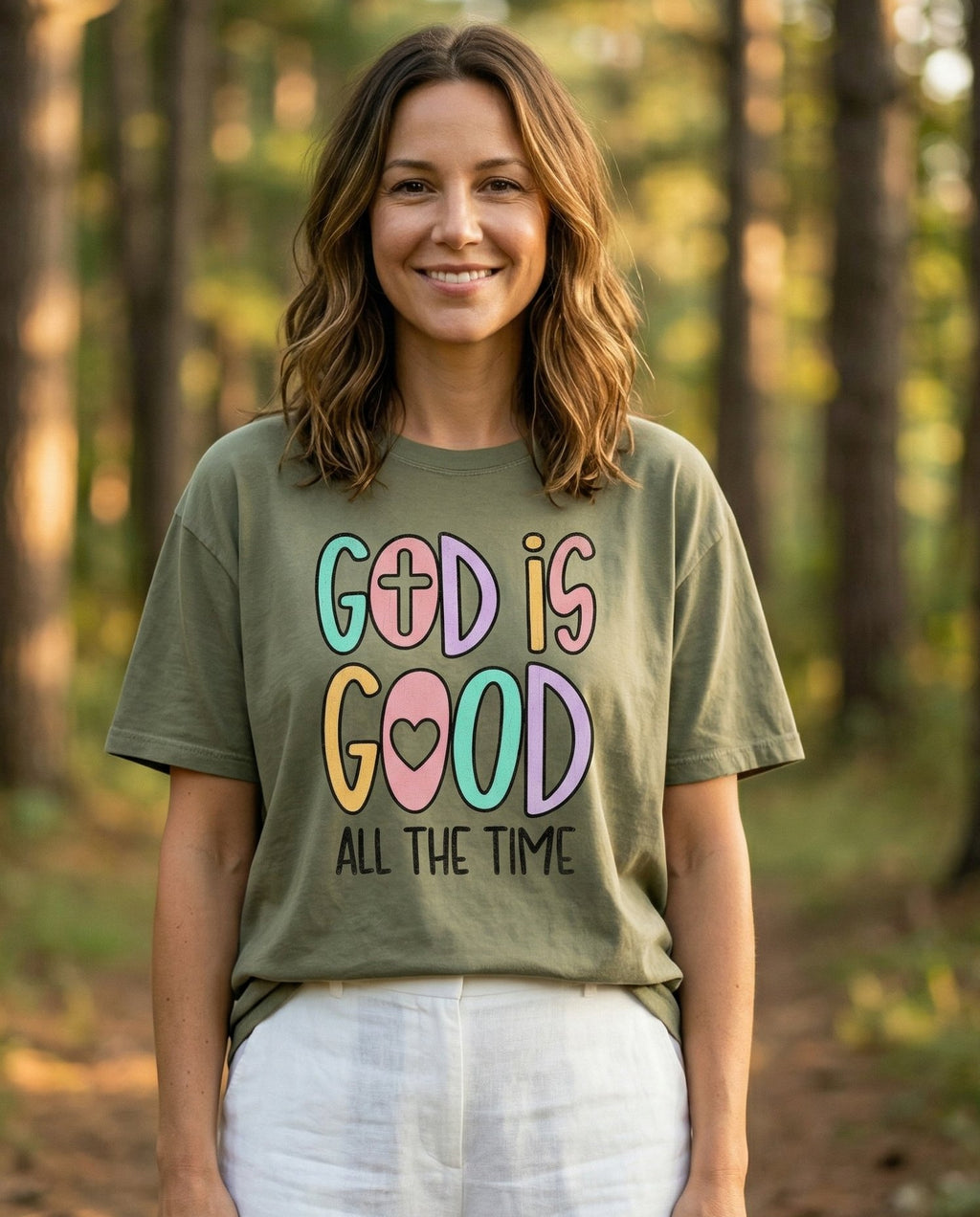 God is Good Joyful – Sage women's Christian tee, lifestyle photo in nature trail – Playful colorful bubble-letter 'GOD IS GOOD' with cross and heart acce – She Wears Faith