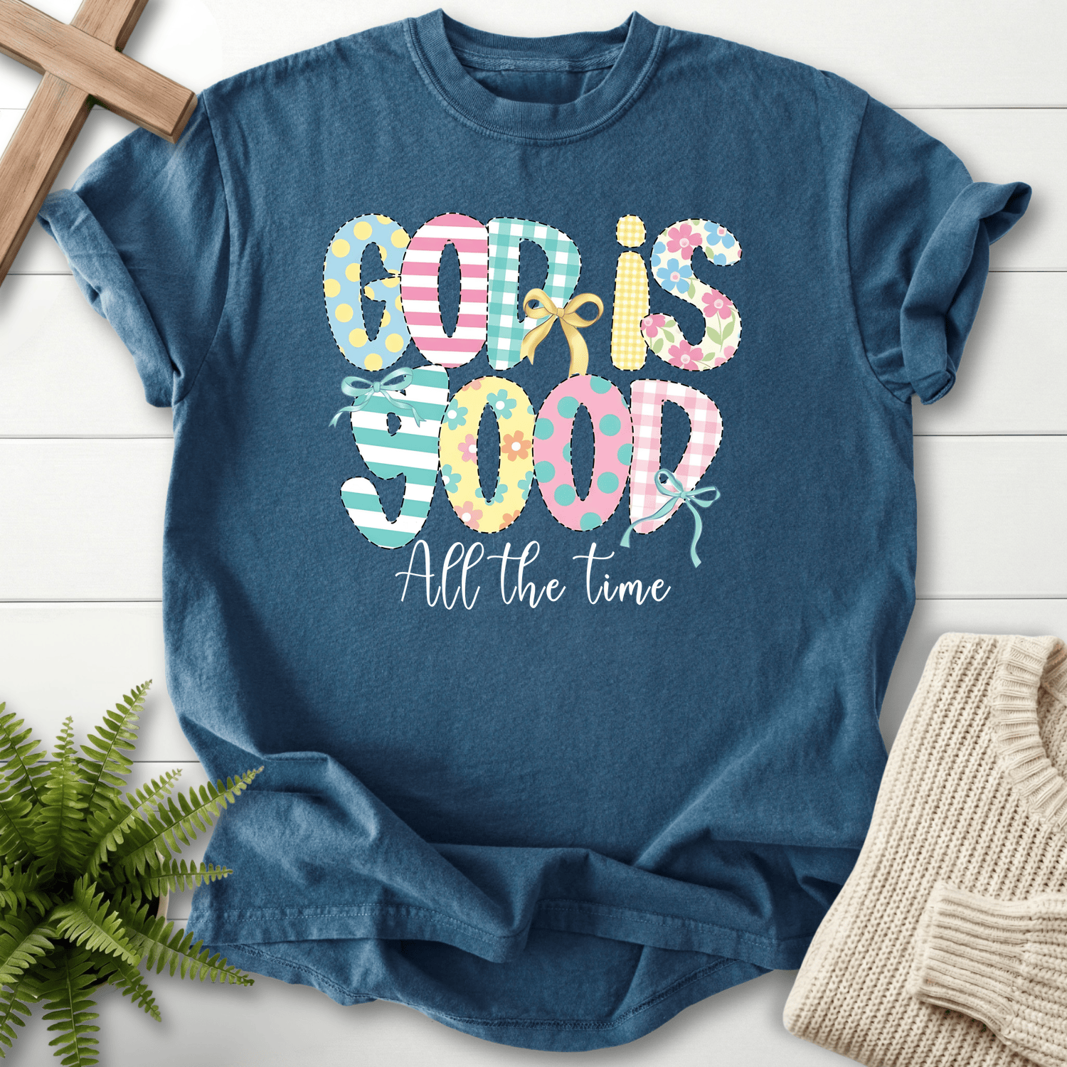 Midnight blue Bible verse tee with pastel patchwork 'God Is Good All The Time' in mixed patterns and a bow accent.