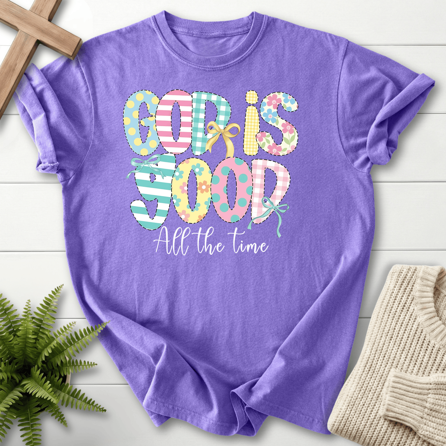 Violet women's faith t-shirt with playful patchwork 'God Is Good' lettering in pastel stripes and polka dots.