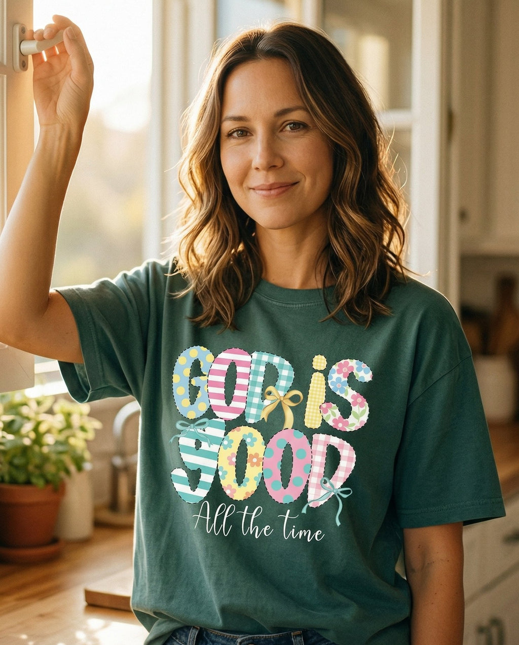 God is Good Patchwork – Blue Spruce women's Christian tee, lifestyle photo in morning kitchen setting – Patchwork-style 'GOD IS GOOD' letters in mixed patterns including stri – She Wears Faith