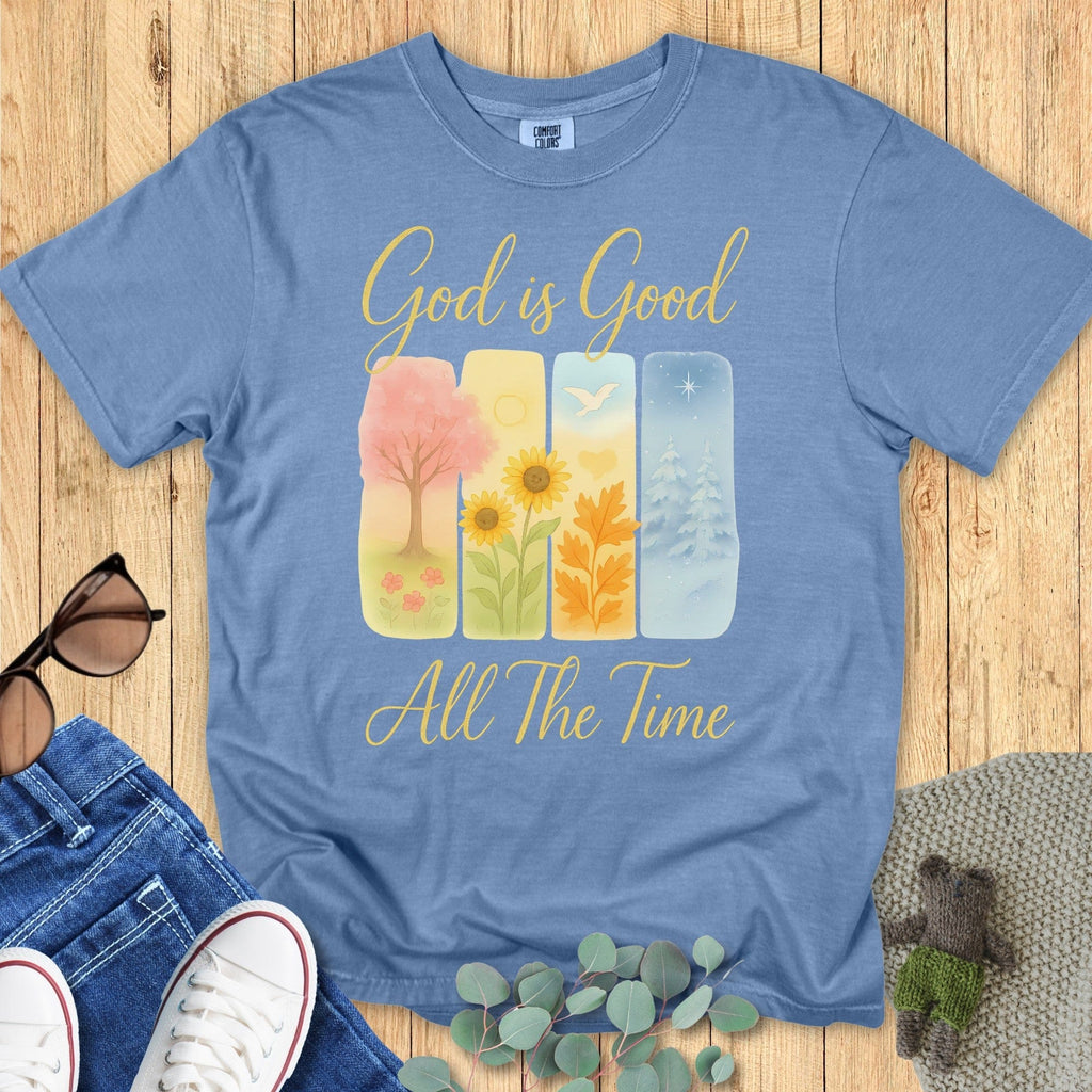 Comfort Colors 1717 Christian women t-shirt in blue jean, decorated with the Christian message "God is Good All The Time." The design includes four illustrated panels representing the seasons, symbolizing God's goodness year-round. Displayed in a casual flat lay with denim and accessories