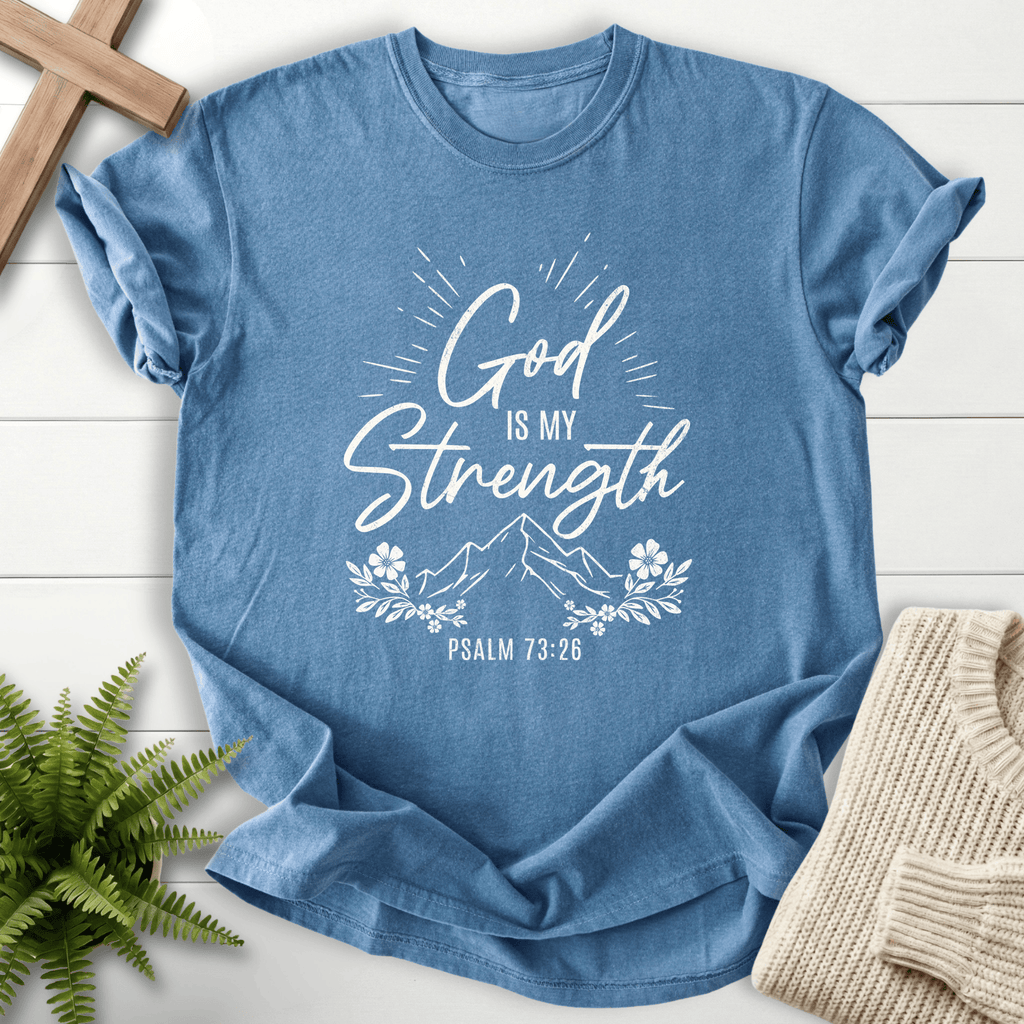 Blue Jean Bible verse tee with glowing 'God Is My Strength' script, a mountain peak, and a floral frame, inspired by Psalm 73:26.