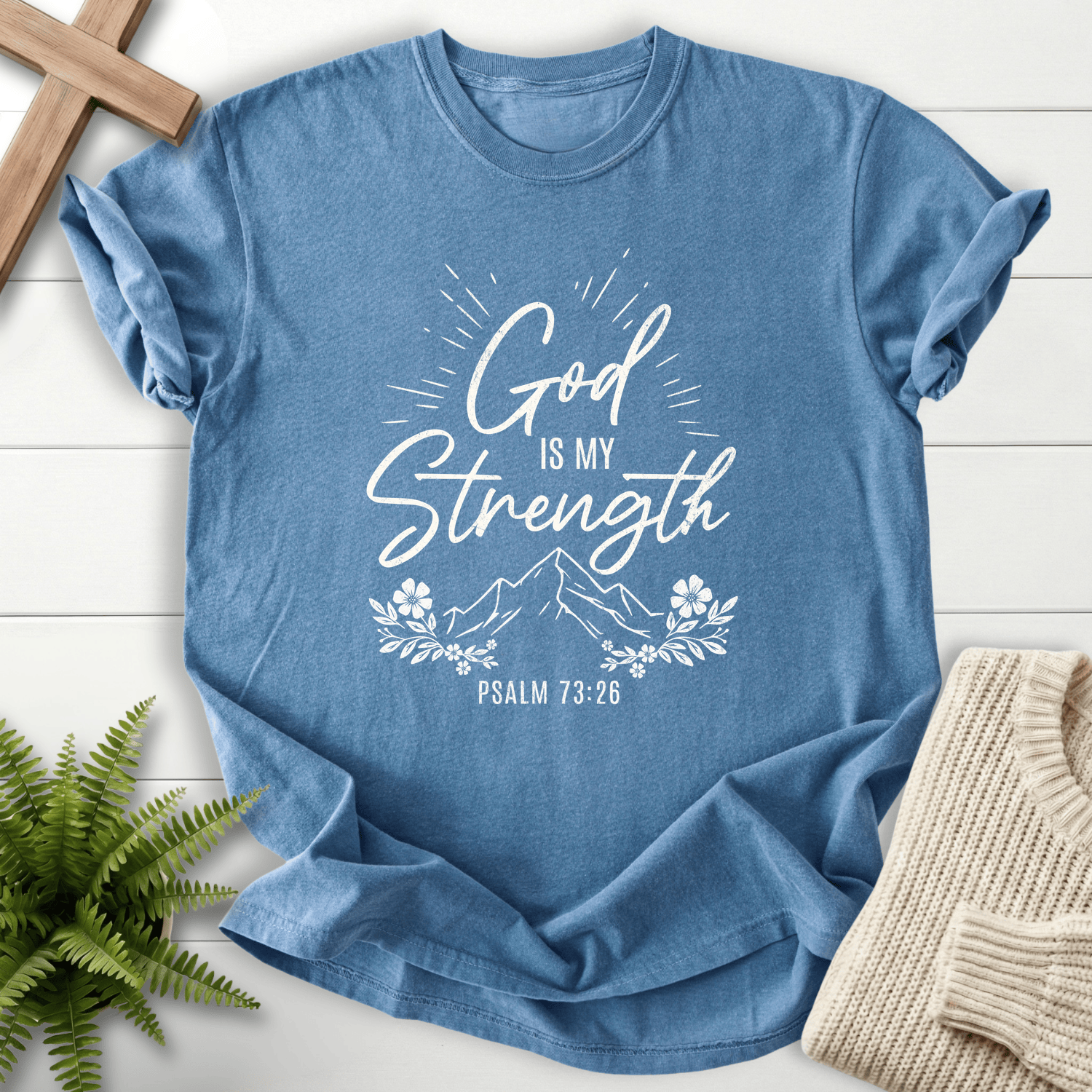Blue Jean Bible verse tee with glowing 'God Is My Strength' script, a mountain peak, and a floral frame, inspired by Psalm 73:26.