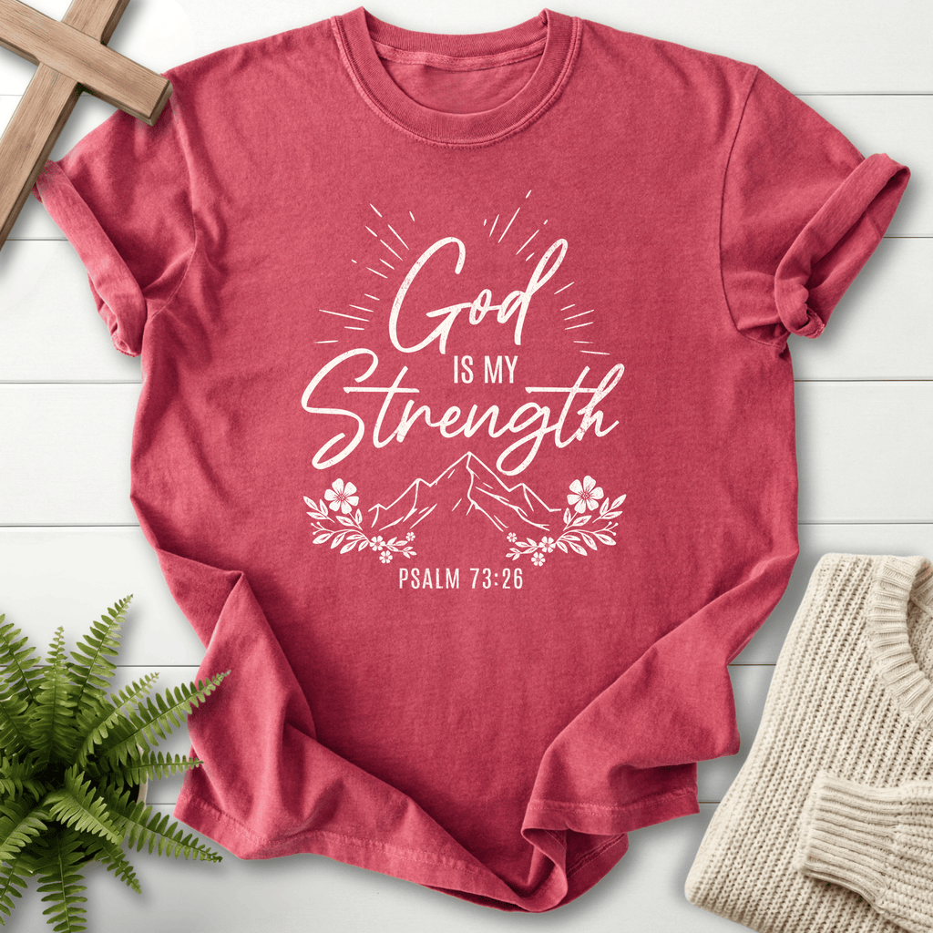 Crimson Bible verse tee with bold 'God Is My Strength' script, a sunburst effect, and a flower border, inspired by Psalm 73:26.