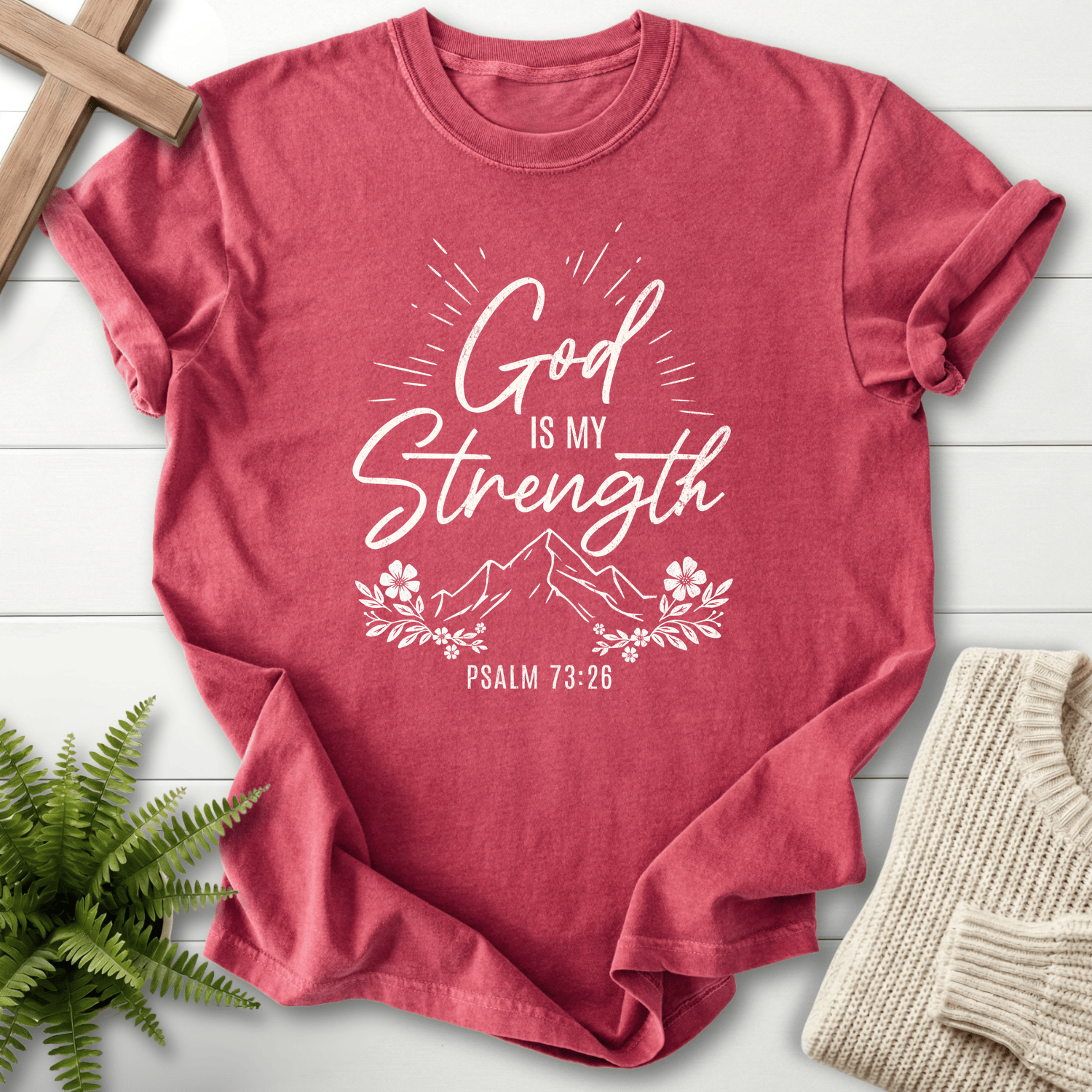 Crimson Bible verse tee with bold 'God Is My Strength' script, a sunburst effect, and a flower border, inspired by Psalm 73:26.