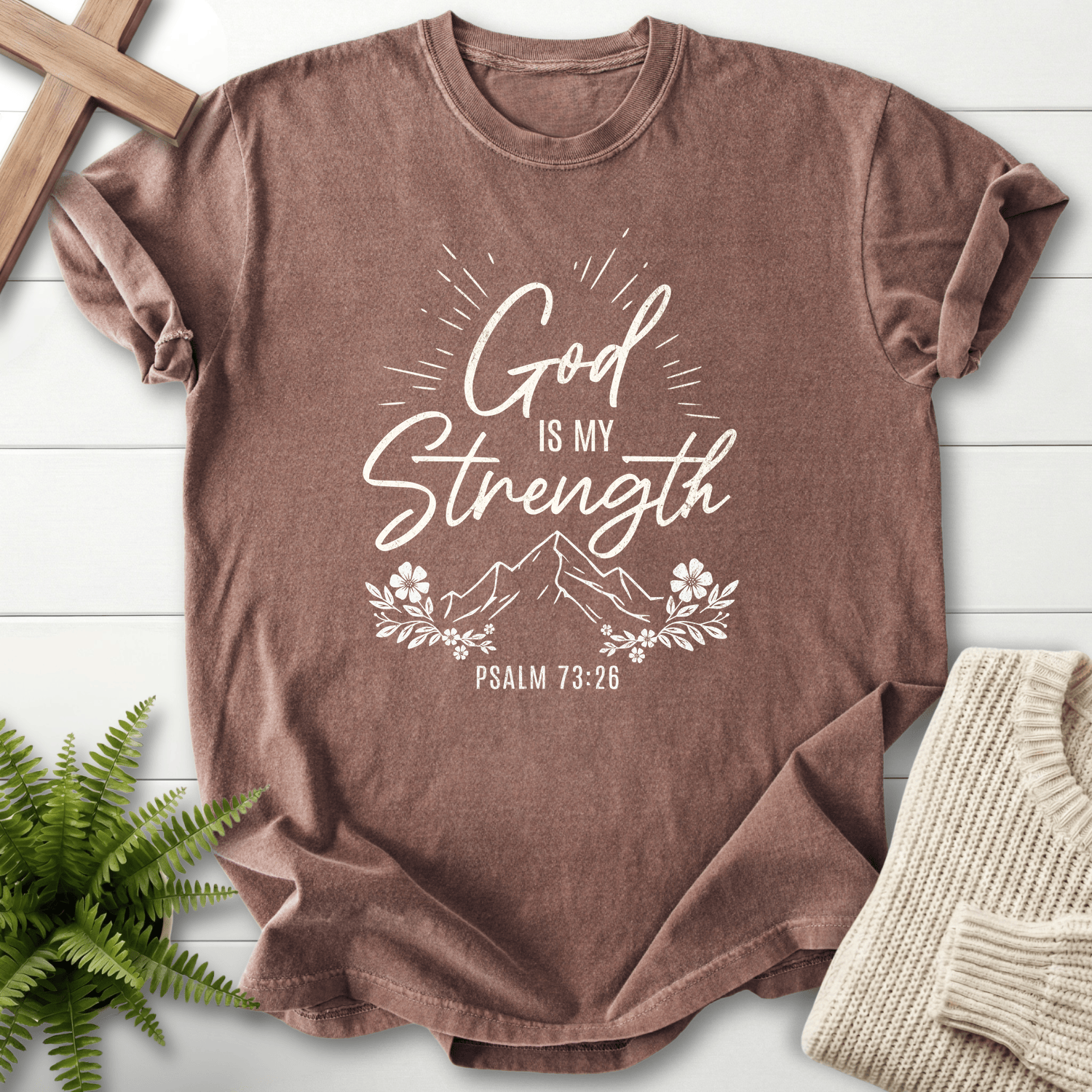 Espresso Bible verse tee with radiant 'God Is My Strength' lettering, a mountain graphic, and wildflower accents, inspired by Psalm 73:26.