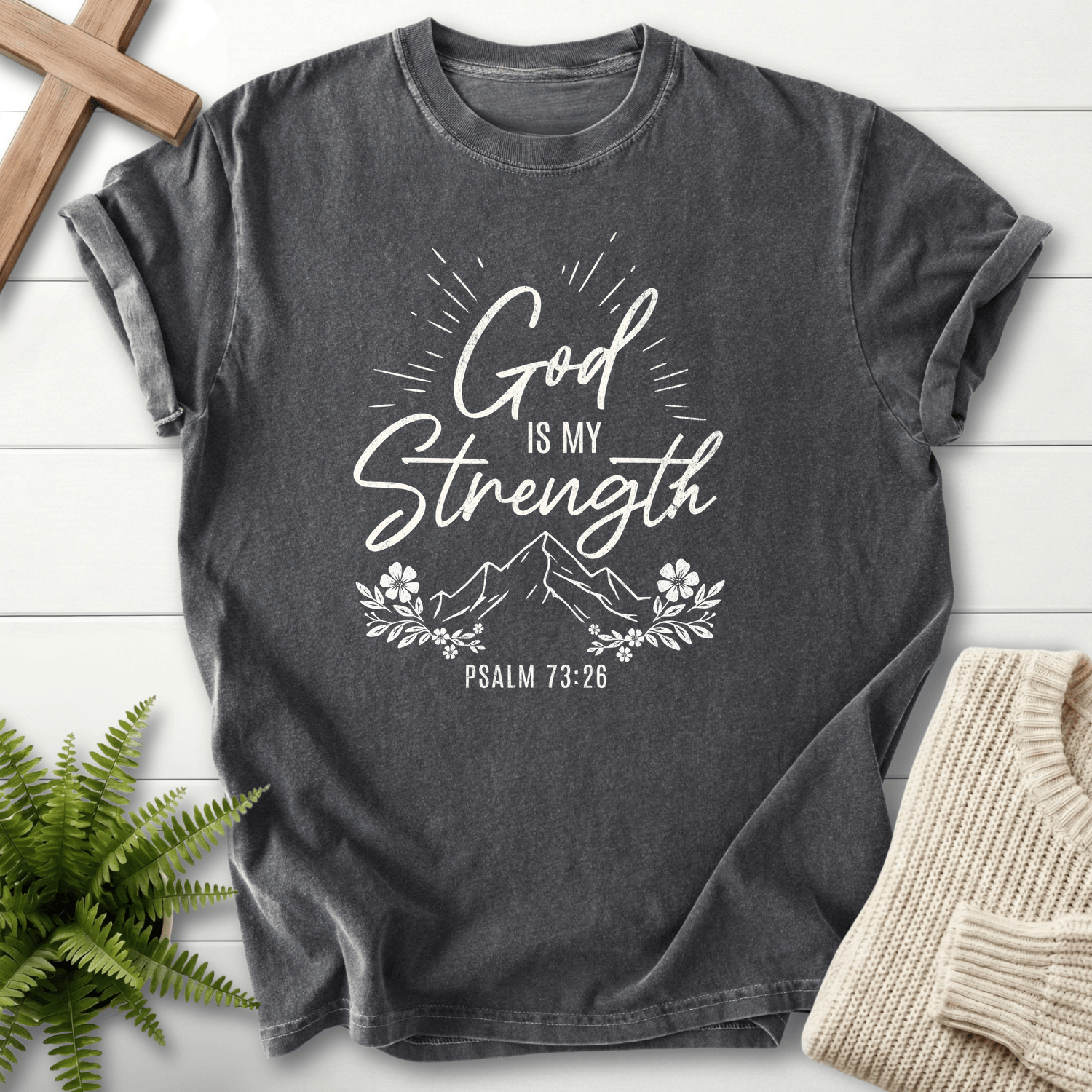 Pepper women's faith t-shirt with bright white 'God Is My Strength' script and a mountain floral design, inspired by Psalm 73:26.