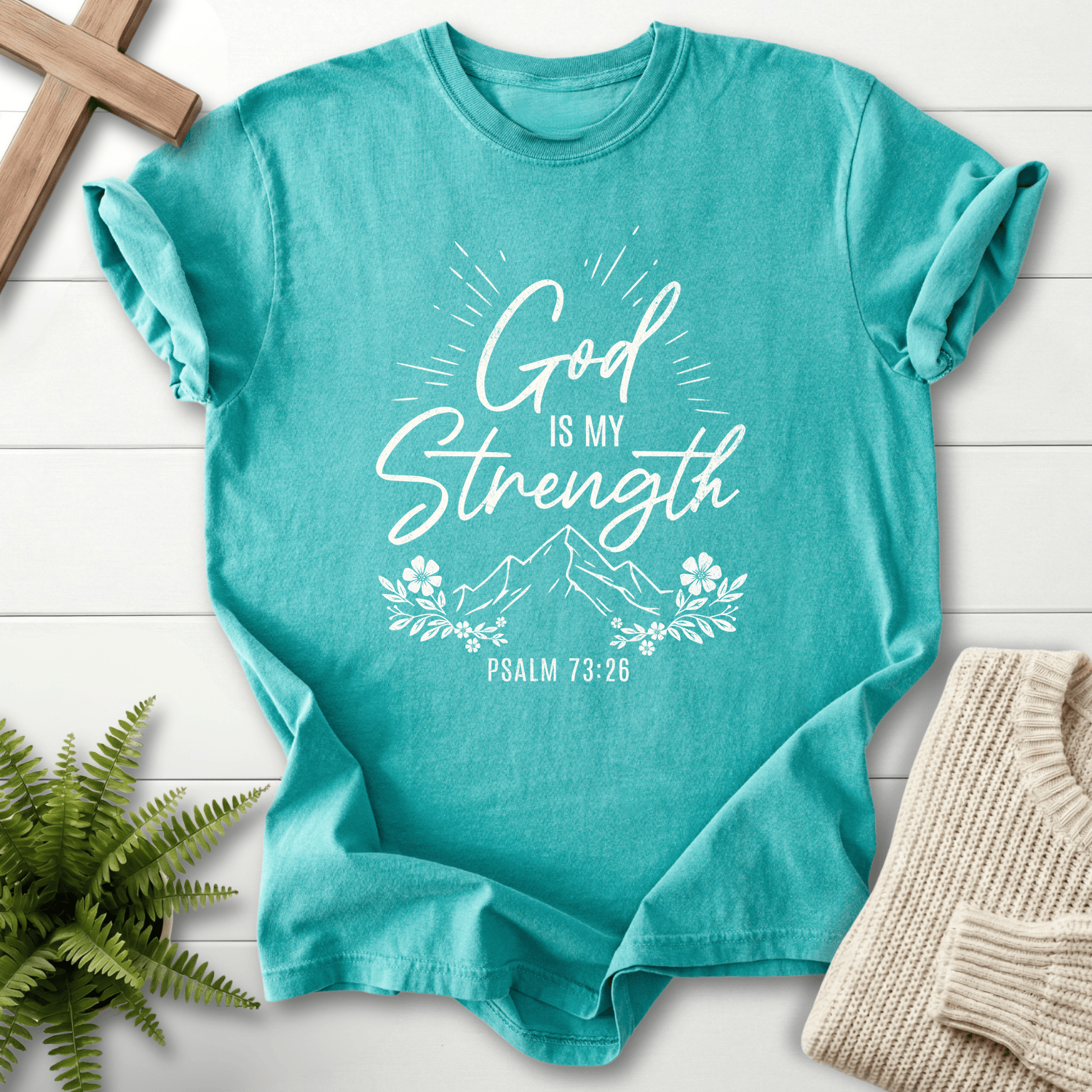 Seafoam Bible verse tee with 'God Is My Strength', a light burst, and floral sprigs, inspired by Psalm 73:26.