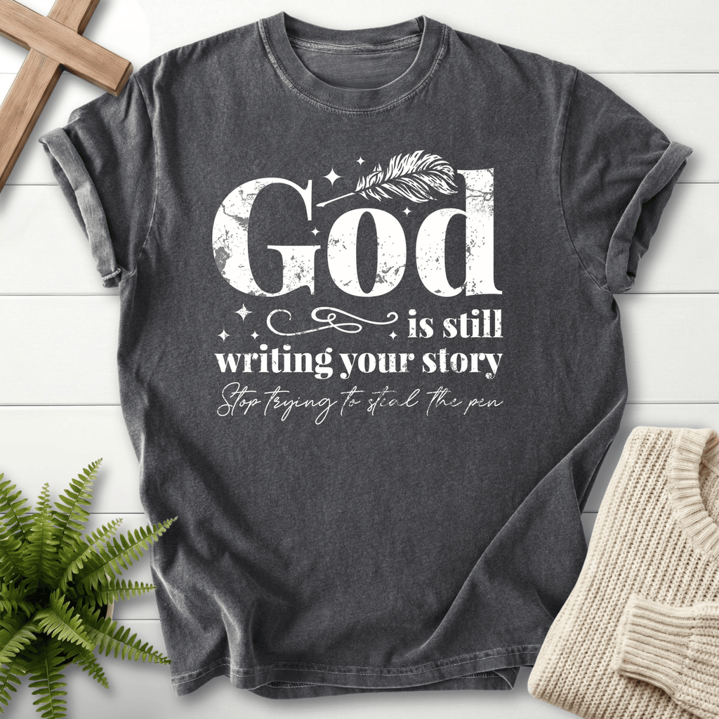 Pepper women's faith t-shirt with bold 'God is Still Writing Your Story' and a feather pen graphic.