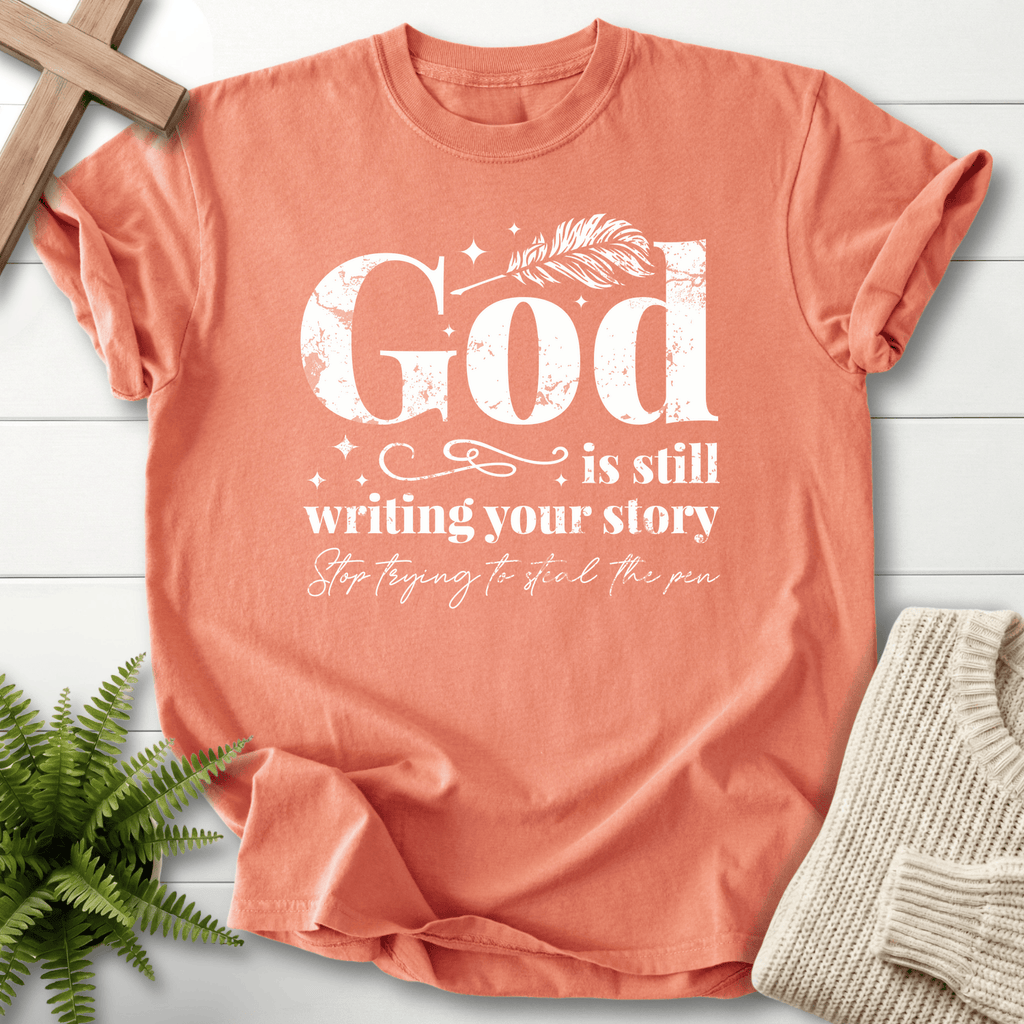 Terracotta women's faith t-shirt with distressed 'God is Still Writing Your Story' and the phrase 'Stop trying to steal the pen'.