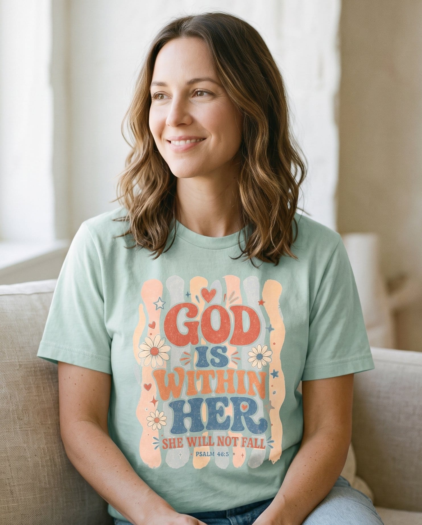 God Is Within Her Retro – Bay women's Christian tee, lifestyle photo in cozy living room – Retro groovy lettering "God Is Within Her – Psalm 46:5 – She Wears Faith