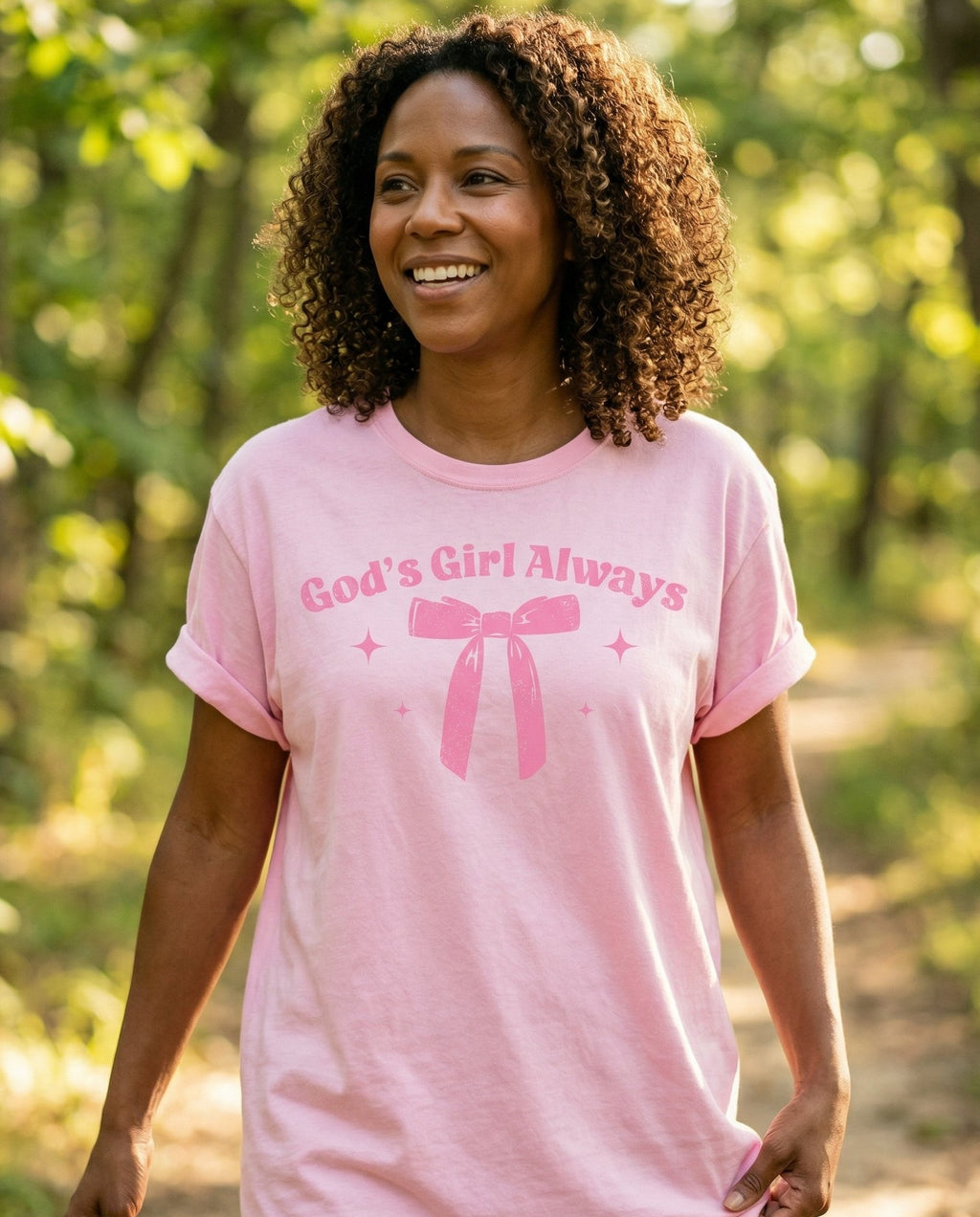 God's Girl Always Bow – Blossom women's Christian tee, lifestyle photo in nature trail – Curved 'God's Girl Always' text above a large illustrated ribbon bow w – She Wears Faith