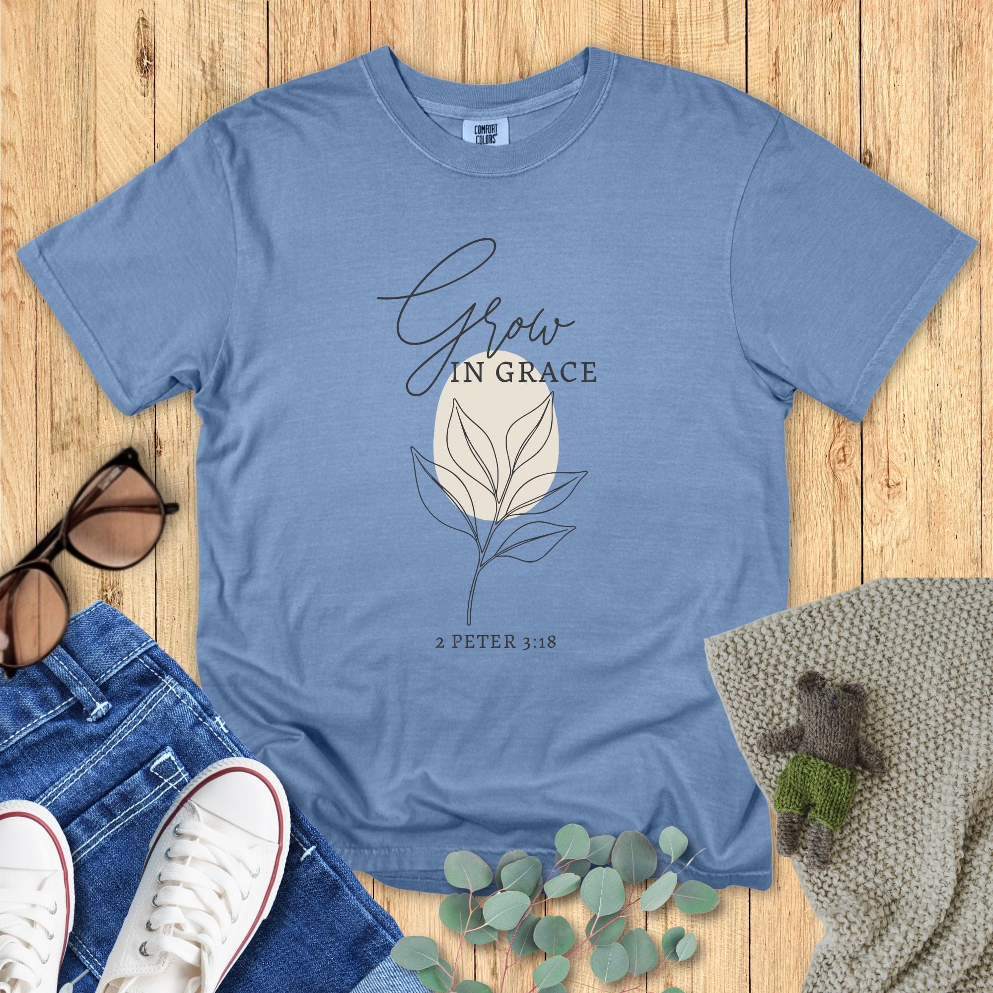 Flatlay of a Comfort Colors 1717 blue jean “Grow in Grace – 2 Peter 3:18” t-shirt showcasing elegant hand-drawn leaves and cursive lettering. A stylish women’s scripture tee — inspiring faith-based apparel for women and modern Christian shirt, lovely Christian mom gift idea.