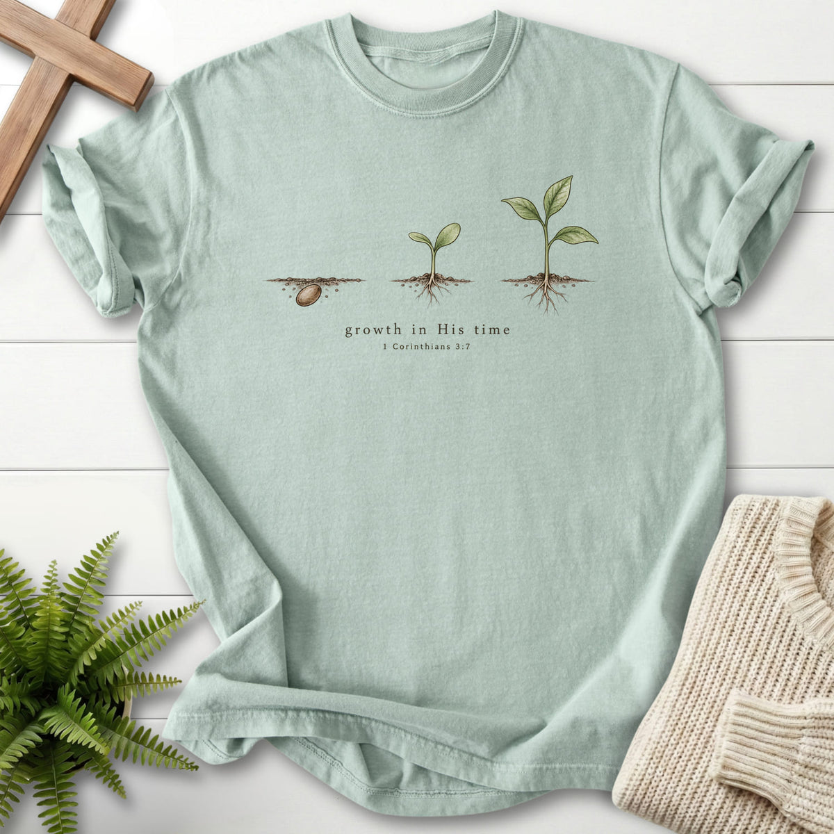 Flat lay of a Bay women's Christian tee featuring "Growth in His Time T-Shirt" 1 Corinthians 3:7.