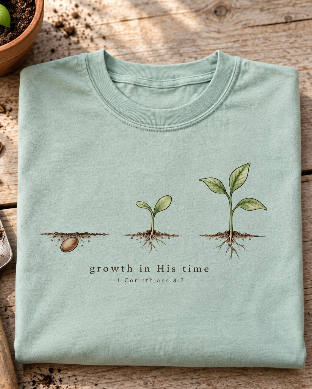 Growth In His Time, Bay women's Christian tee, folded flat lay, Watercolor seed and sprout and leafy plant growth stages, 1 Corinthians 3:7, She Wears Faith