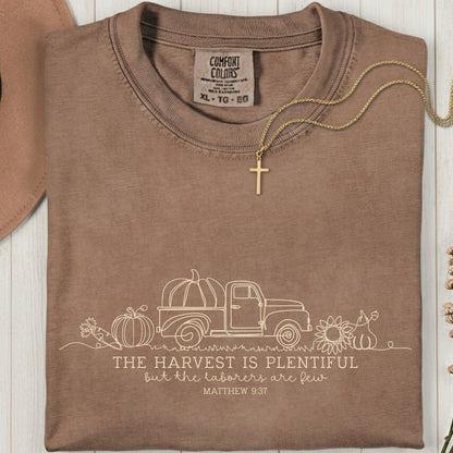Folded Comfort Colors 1717 espresso “The harvest is plentiful but the laborers are few” t-shirt (Matthew 9:37) with gold cross necklace on top. A rustic women’s scripture tee - faith-based apparel for women and modern Christian shirt, cozy Christian mom gift idea for autumn.