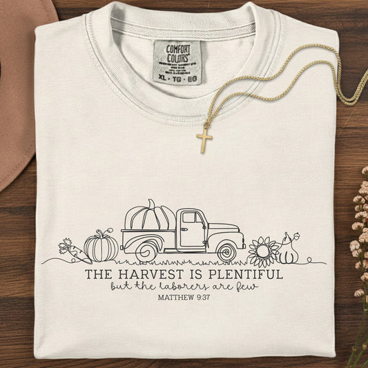 Folded Comfort Colors 1717 ivory “The harvest is plentiful but the laborers are few” t-shirt (Matthew 9:37) styled with gold cross necklace. A neutral women’s scripture tee -  faith-based apparel for women and modern Christian shirt, timeless Christian mom gift idea for the season.