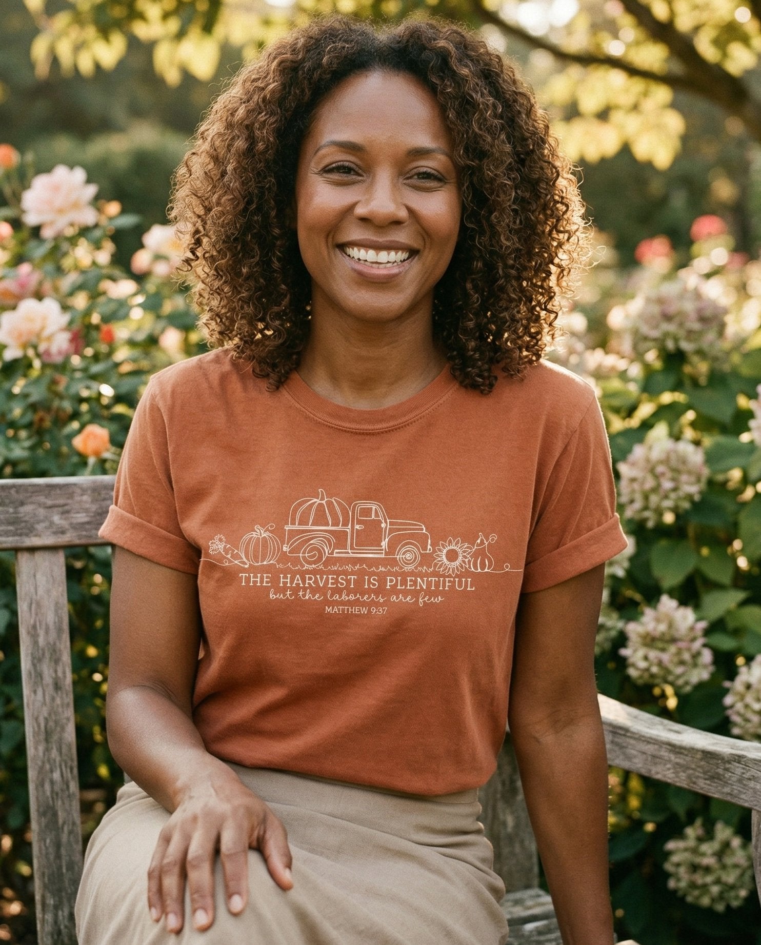 Harvest Is Plentiful – Yam women's Christian tee, lifestyle photo in outdoor garden – Line-art vintage farm truck loaded with pumpkins and sunflowers – Matthew 9:37 – She Wears Faith