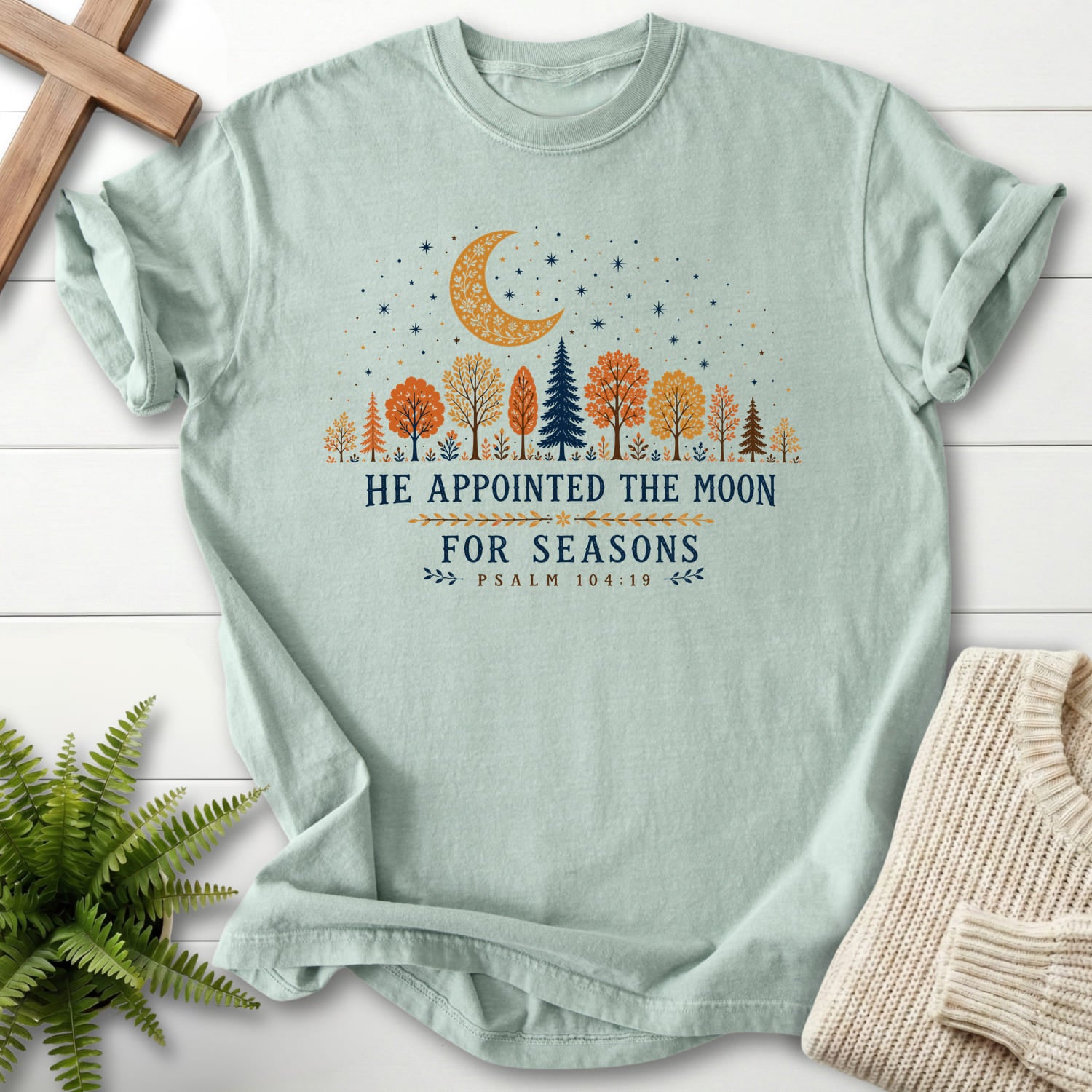 Flat lay of a Bay Scripture shirt featuring floral line art with "He Appointed the Moon for Seasons T-Shirt" Psalm 104:19.