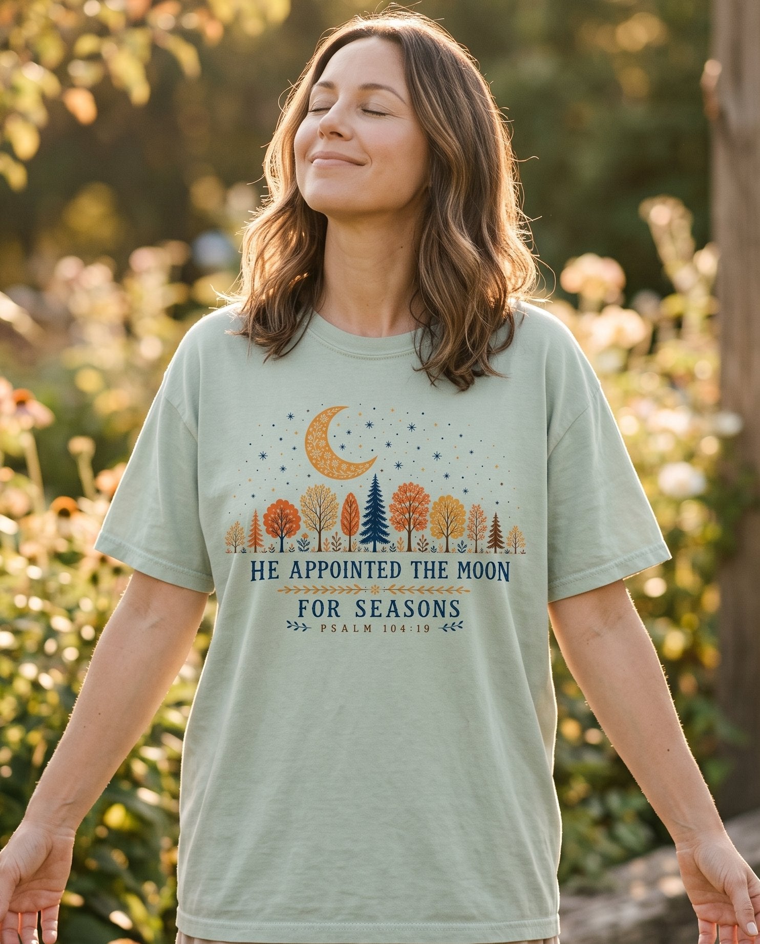 He Appointed the Moon – Bay women's Christian tee, lifestyle photo in outdoor garden – Night-sky scene with autumn trees and a floral crescent moon – Psalm 104:19 – She Wears Faith