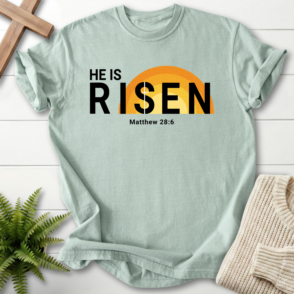 Bay Bible verse tee with bold 'He Is Risen' Easter design and an orange sun rising graphic, inspired by Matthew 28:6.