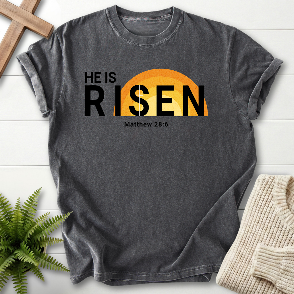 Pepper Bible verse tee with modern 'He Is Risen' lettering and a radiant orange-gold sun design, inspired by Matthew 28:6.