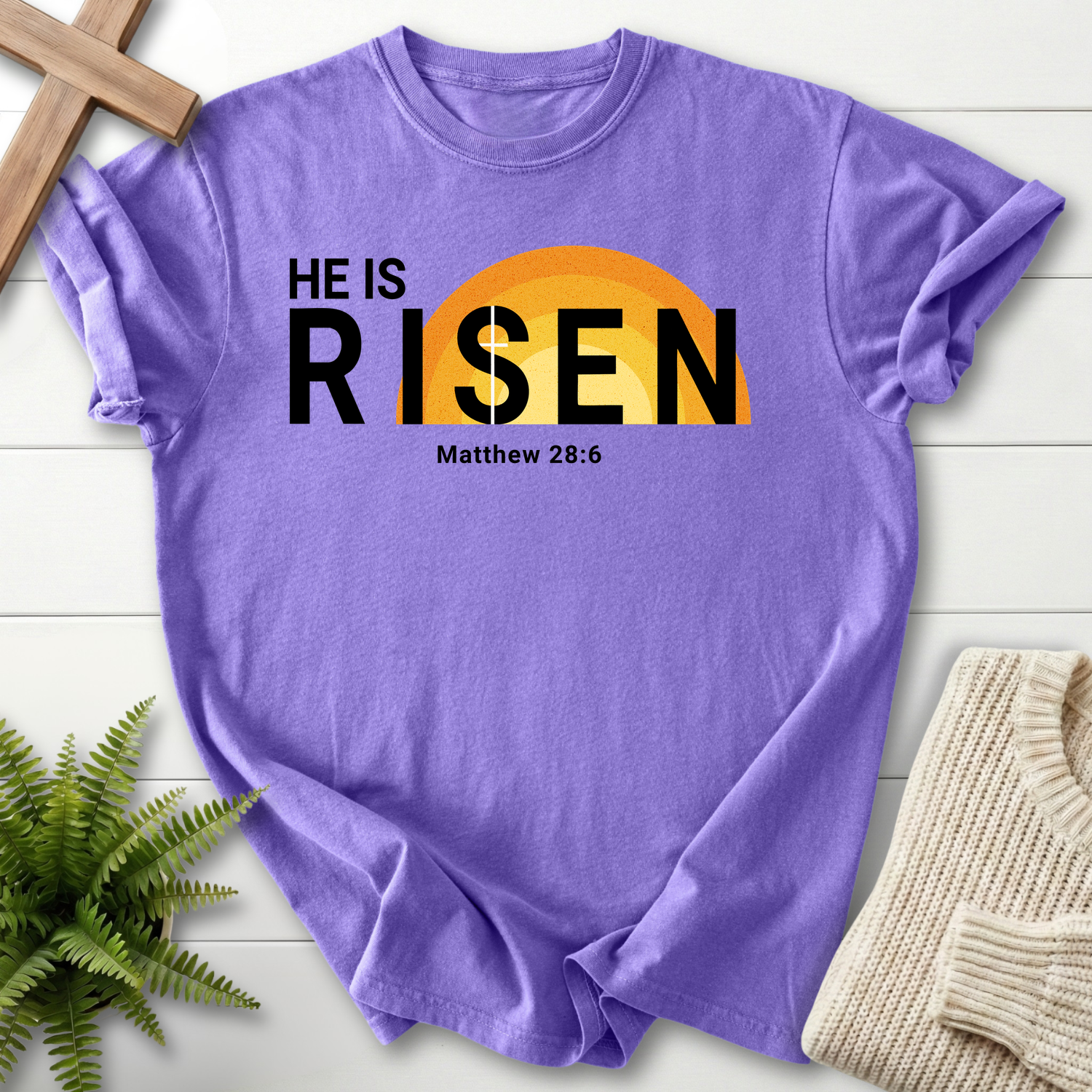 Violet Bible verse tee with 'He Is Risen' overlaid on a golden sunrise, inspired by Matthew 28:6.