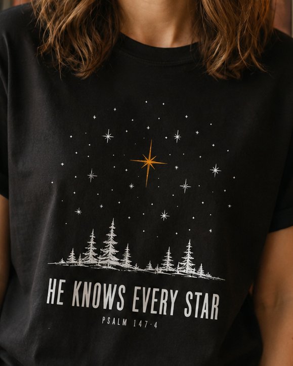 HE Knows Every - Black women's Christian tee, lifestyle photo in cozy reading nook - Engraved starry night sky over a mountain valley - Psalm 147:4 - She Wears Faith