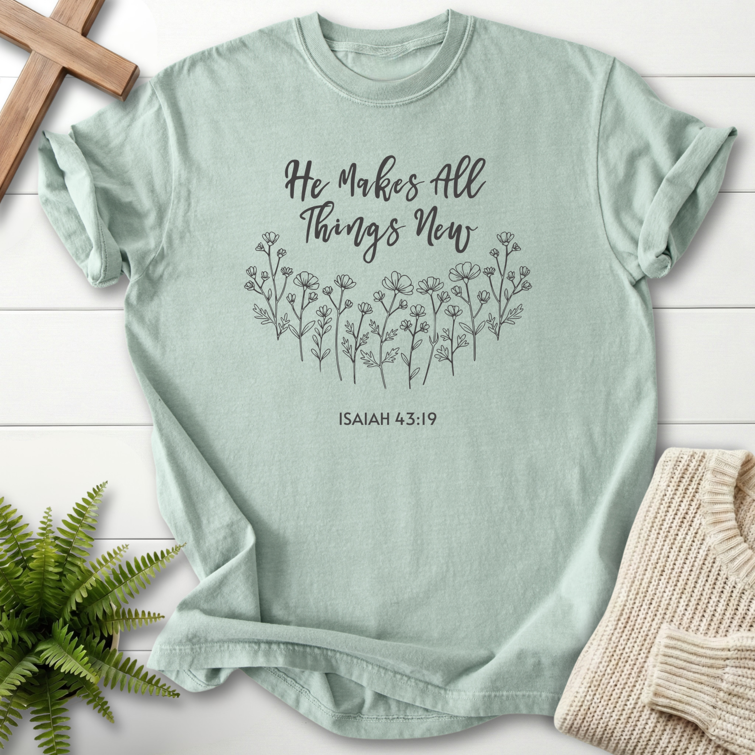 Bay women's faith t-shirt with delicate wildflower line art and 'He Makes All Things New' script, inspired by Isaiah 43:19.
